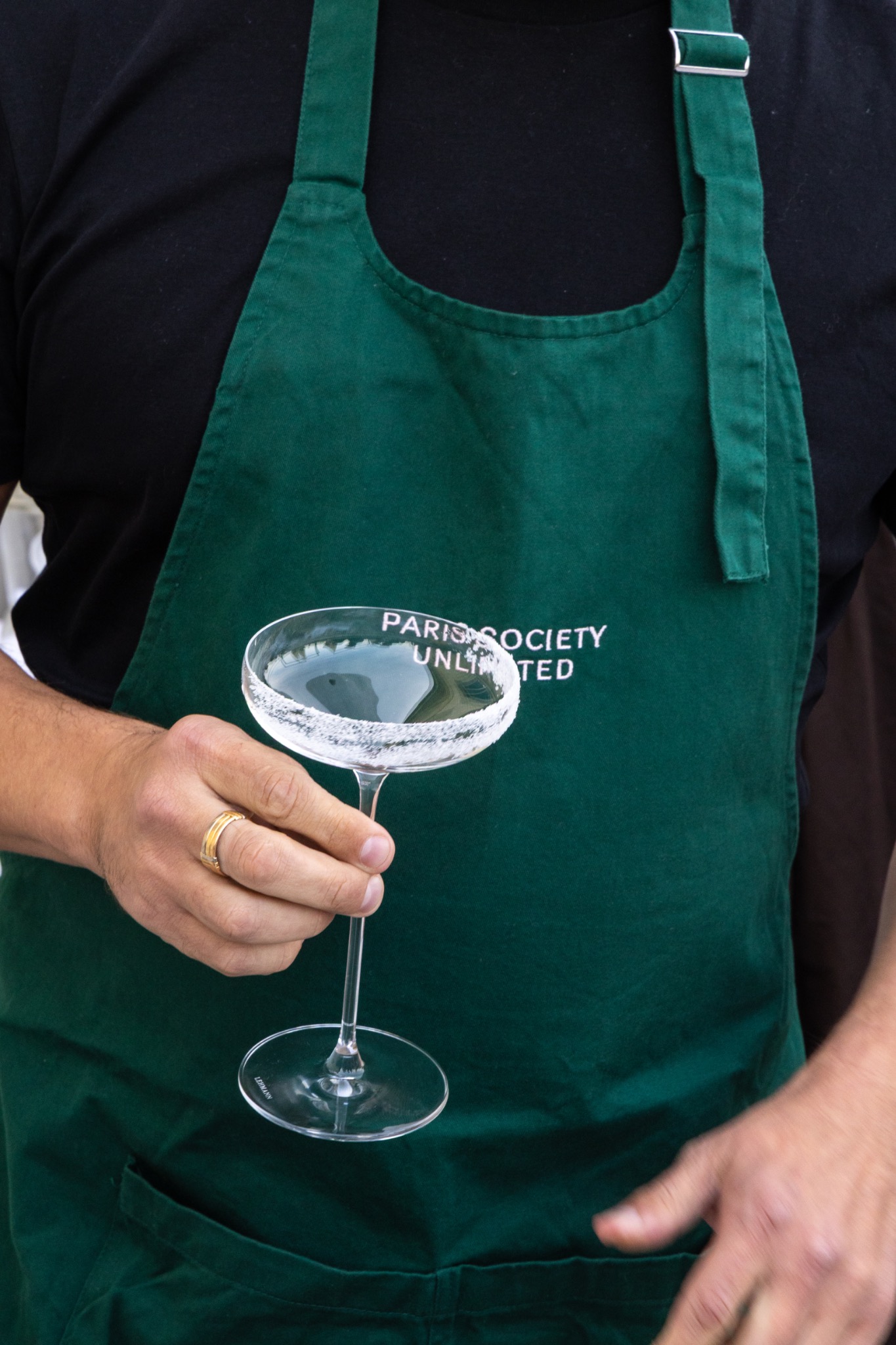 Détail d’un verre tenu par un barman en tablier vert